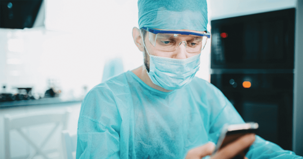 Young surgeon looking at smartphone in operating room.